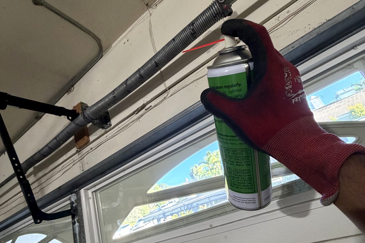 Technician lubricating a garage door spring during a tune-up